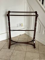 Wooden blanket rack standing on tiled floor near a white wall and staircase. Shows full rack from the front.