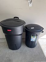 Two black plastic garbage bins, larger Rubbermaid with wheels and smaller unbranded