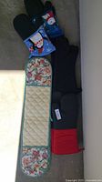 All mitts laid out: floral double glove, two blue holiday mitts, two black mitts, black/red mitt