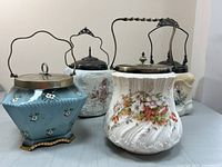 Four antique biscuit barrels arranged together showing different shapes, colors, metal lids, and handles