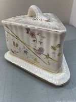 Side view of the triangular porcelain covered cheese dish showing floral decoration and gilded trim.
