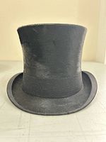 Front view of tall black fur top hat with slightly curved brim on white surface.