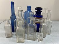 Twelve assorted antique glass bottles in clear and blue glass displayed on a table