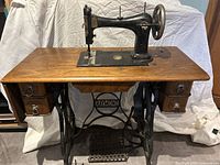 Full view of the antique Raymond cast iron treadle sewing machine mounted on a wooden table with four drawers and a cast iron treadle pedal mechanism.