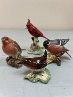 Four detailed porcelain bird figurines on table, showing full group including red cardinal, brown robin, and others.