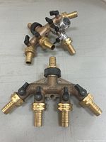 Two brass 4-way manifolds showing four shut off valves and barbed hose fittings. Manifolds positioned on a surface to display multiple connection points.