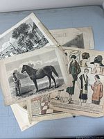 Top view of assorted antique prints, showing horse print on top and some fashion plates underneath