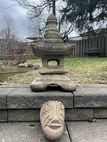 Concrete pagoda on stone ledge next to carved stone face sculpture, showing overall structure and size.