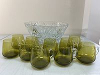 Clear glass punch bowl and 10 vintage green punch glasses with handles, showing overall lot contents and glassware condition