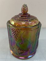 Front and side view of carnival glass jar with lid showing the grape cluster and leaf embossing and iridescent finish.