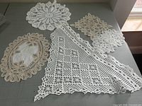 Five hand crocheted doilies arranged on a surface showing various shapes and intricate lace designs in white and off-white.
