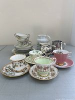 Mixed lot of china teacups stacked and arranged showing various floral and gold decorative patterns