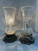 Two vintage lamps with detailed cut glass shades and ornate brass bases, plugged in and illuminated.