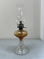 Full view of the oil lamp showing clear glass base, amber glass font, metal burner, and chimney.
