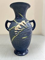 Front view of blue Roseville pottery vase with relief freesia flowers and two handles.
