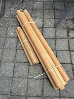 Bundles of turned pine doweling rods of different lengths placed on pavement.