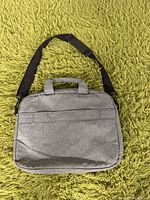Front view of the grey Lenovo laptop bag placed on a green carpet. Shows handles and adjustable black shoulder strap.