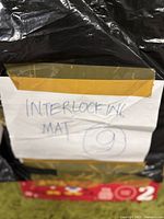 Photo showing handwritten label 'INTERLOCKING MAT 9' taped on a box wrapped in black plastic.