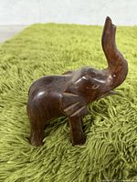 Photo of dark brown hand-carved wooden elephant figurine with raised trunk, placed on green shag carpet.