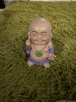 Front view of the Laughing Buddha figurine showing smiling face, gold necklace, green pendant, and purple garments