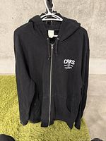 Full front view of black zip-up hoodie with hood, hanging on hanger showing size and condition.