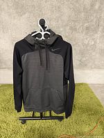 Front view of Nike men's hoodie showing grey body, black sleeves, and hood with drawstrings and front kangaroo pocket.