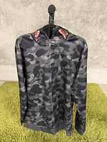 Front view of men's hoodie showing black and gray camouflage pattern and front zipper.