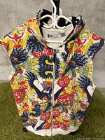 Front view of the sleeveless hoodie with zipper and colorful pattern displayed on a hanger.