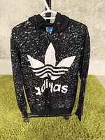 Front view of black Adidas hoodie with white splatter pattern and large trefoil logo