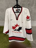 Front full view of the white Canada hockey jersey showing large red and black maple leaf logo and size tag.