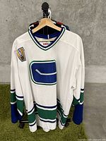 Full view of white hockey jersey by CCM with Vancouver Canucks logo, blue and green detailing and patch on shoulder.