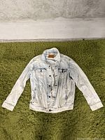 Front view of light wash denim Levi Strauss jean jacket laid flat on green carpet, showing button closure, pockets, and collar with leather brand patch.