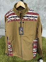 Brown men’s jacket with patterned fabric accents on shoulders and pockets, hanging on a hanger against a wall.