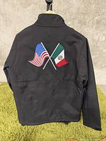 Back view of black jacket showing crossed embroidered American and Mexican flags