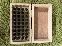 Open wooden box displaying 26 black metal letter and number punches placed upright in slots.