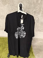 Front view of new black XL T-shirt with white graphic of skull wearing sunglasses riding a motorcycle.