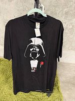 Photo of the black T-shirt hanging on a hanger showing the front graphic of Darth Vader and a red rose.