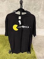 Front view of the new black XL t-shirt hanging on a hanger showing the abstract yellow and white circular design on front.