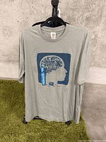 Full view of a light gray XL t-shirt on hanger showing the front graphic of a mechanic working inside a brain silhouette.