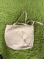 Front view of white leather tote bag with creases and two shoulder straps on green carpet.