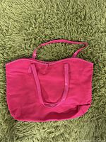 Front view of pink fabric tote bag with longer single strap and softer shape, placed on green shag carpet.