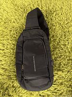 Full view of the black shoulder backpack showing front pocket and single strap.