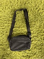 Front view of small black crossbody bag with adjustable strap, showing front zipper pocket.
