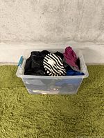 Clear plastic bin containing assorted small/petite women's clothing in various colors and patterns including black, white, purple, blue, and striped items.