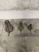 Three metal conical mesh strainers arranged side by side on floor in descending size order