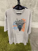 Full front view of gray short sleeve T-shirt hanging on rack, featuring graphic design.
