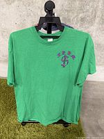 Front view of the green t-shirt on a hanger showing the purple chest graphic.