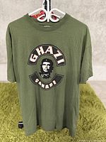 Front view of olive green T-shirt with Ghazi Canada graphic print showing a face and text.