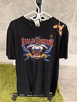 Front view of black Harley-Davidson t-shirt displaying skull graphic and Harley-Davidson logo with bleach/fade spots on right chest area.