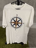 Front view of white T-shirt with compass rose design printed in brown and black.